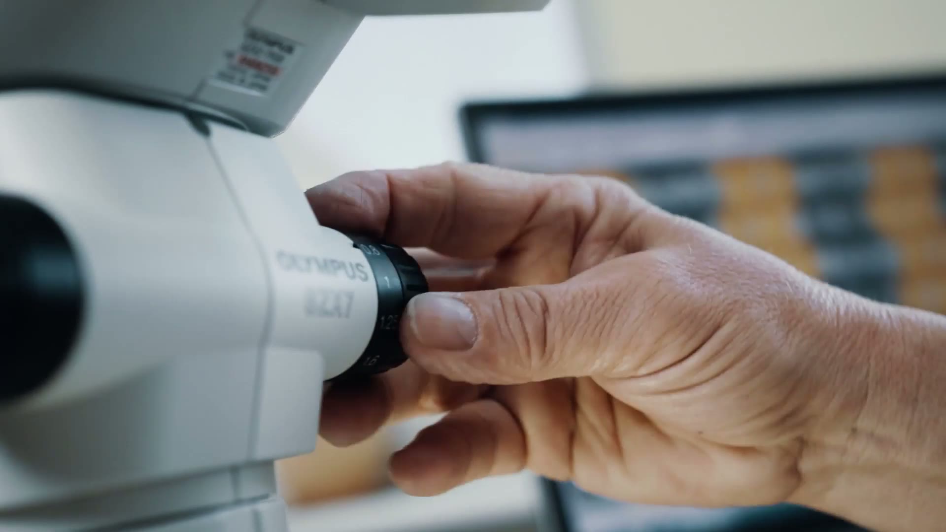 Hand am Mikroskop im Labor – Standbild aus dem Sattler Unternehmensfilm.