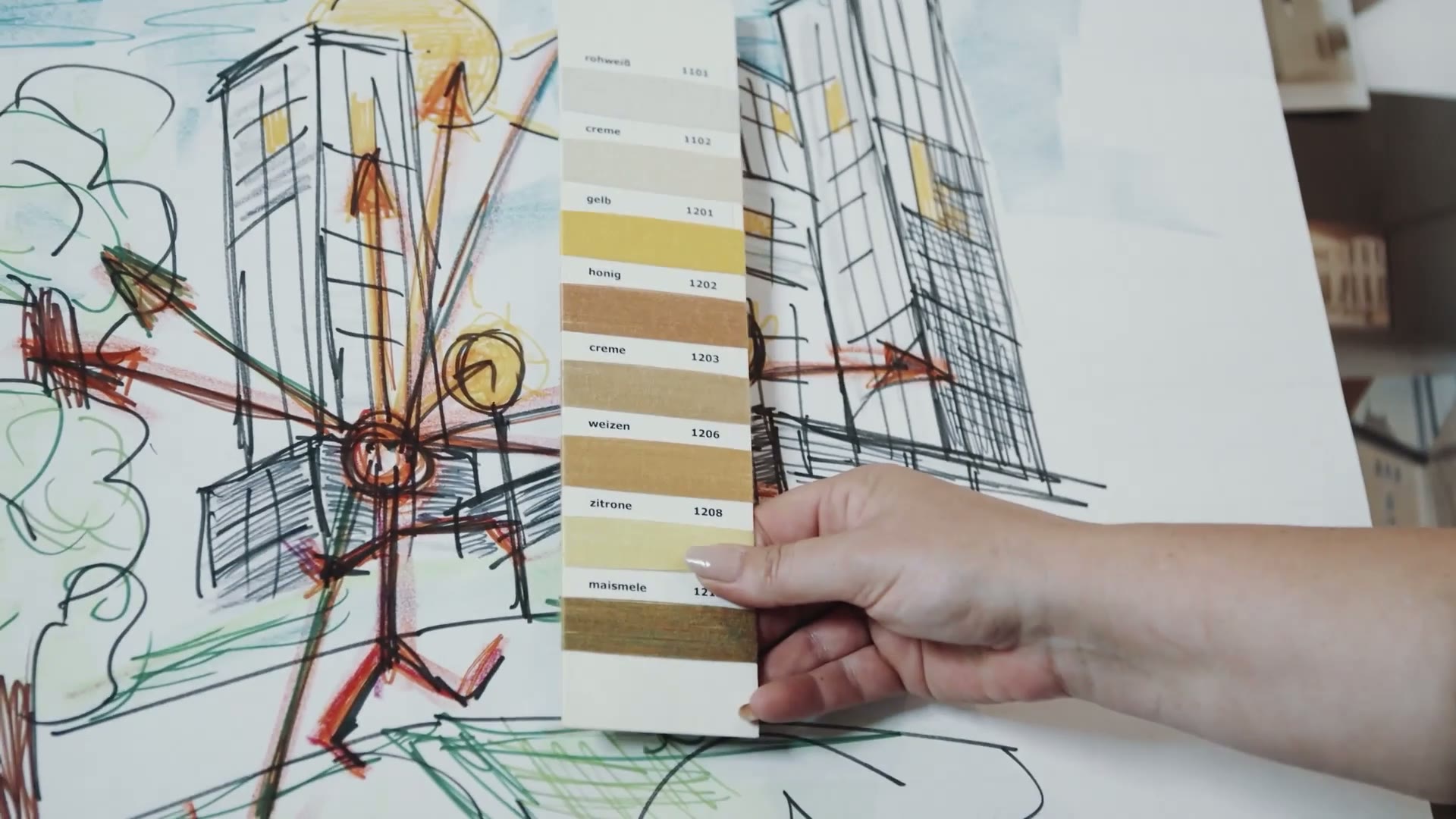 Hand hält eine Farbkarte vor Architekturskizzen – Standbild aus dem Sattler Unternehmensfilm.