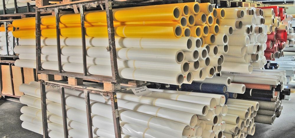 Gestapelte Membranrollen in Weiß, Gelb und weiteren Farben im Lagerregal des SATTLER Factory Outlet Rudersdorf.